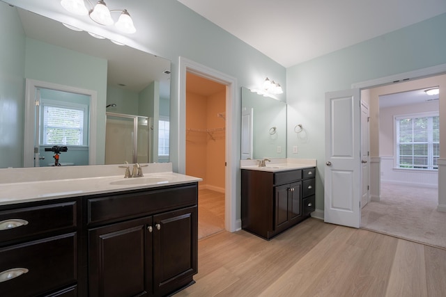 bathroom featuring wood finished floors, a shower stall, two vanities, a spacious closet, and plenty of natural light