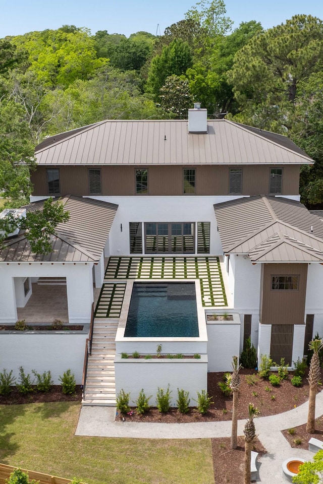 view of front of home with a standing seam roof, metal roof, stairway, and a wooded view
