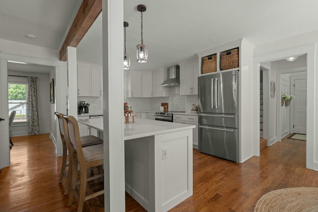 kitchen with backsplash, light countertops, wall chimney exhaust hood, appliances with stainless steel finishes, and a breakfast bar area