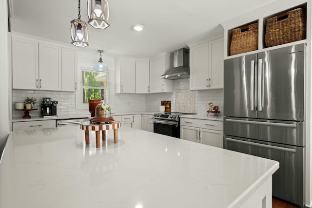 kitchen with wall chimney range hood, tasteful backsplash, stainless steel appliances, decorative light fixtures, and white cabinets