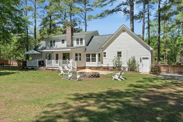 back of property with a fire pit, a chimney, fence, a wooden deck, and a yard