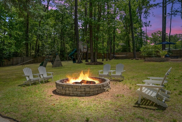 yard at dusk with a fire pit, a fenced backyard, and a playground