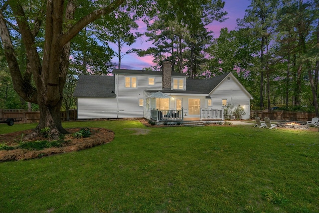 back of property at dusk featuring a fire pit, a lawn, a wooden deck, and fence