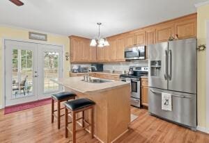 kitchen with light wood-style flooring, a center island with sink, a sink, decorative light fixtures, and stainless steel appliances