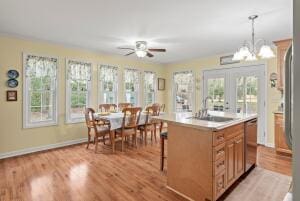 kitchen featuring a sink, light countertops, light wood-style floors, stainless steel dishwasher, and ceiling fan with notable chandelier