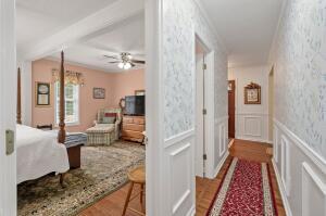 corridor featuring wallpapered walls, a decorative wall, wood finished floors, and wainscoting