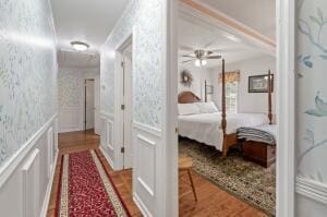 corridor with wallpapered walls, a decorative wall, wood finished floors, and a wainscoted wall