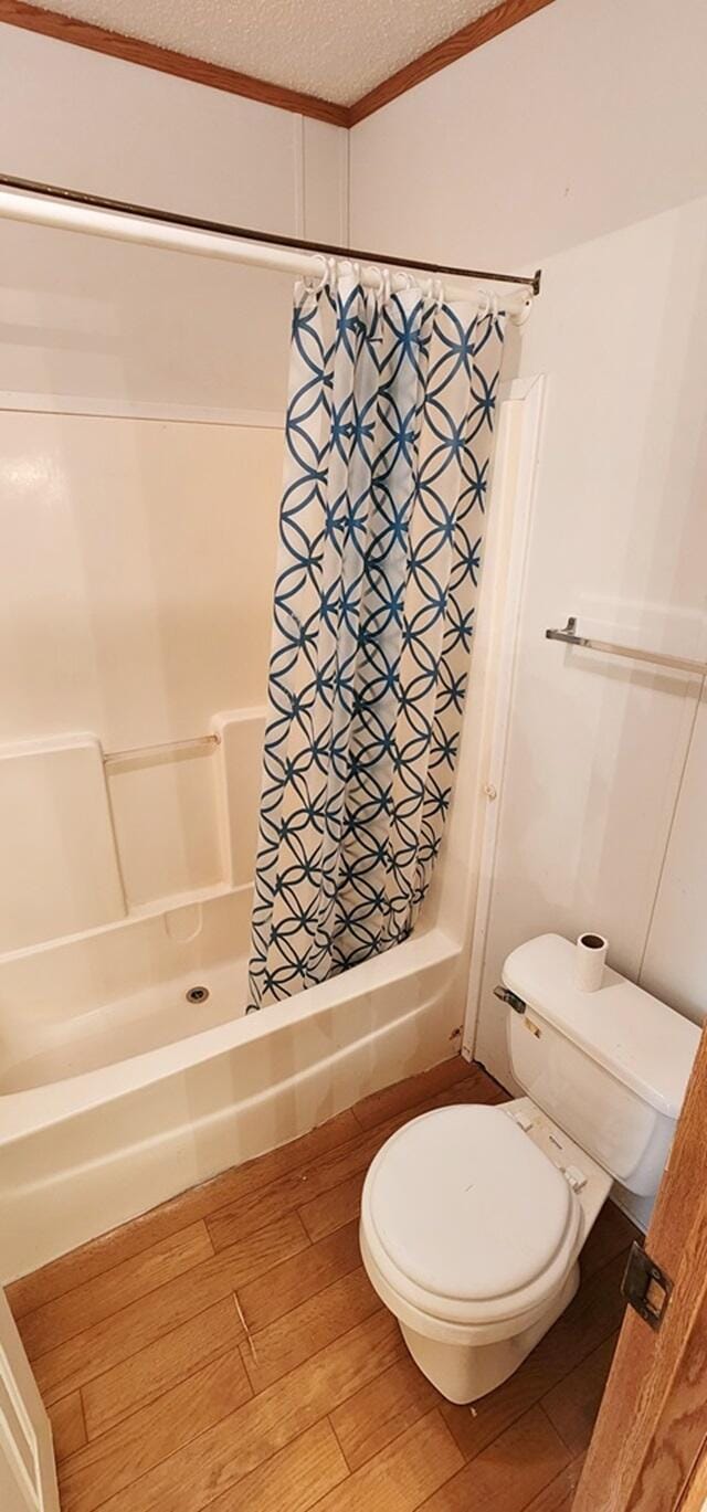 bathroom with shower / bath combination with curtain, ornamental molding, a textured ceiling, hardwood / wood-style flooring, and toilet