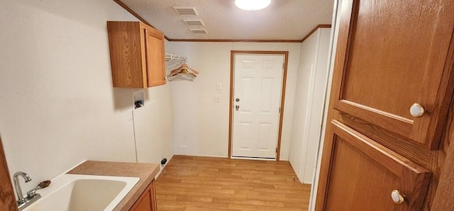 laundry room featuring cabinets, ornamental molding, a textured ceiling, sink, and light hardwood / wood-style floors