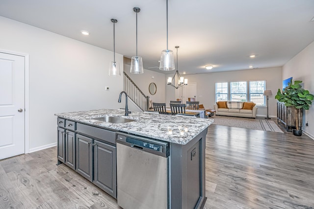 kitchen featuring light stone countertops, a kitchen island with sink, sink, pendant lighting, and dishwasher