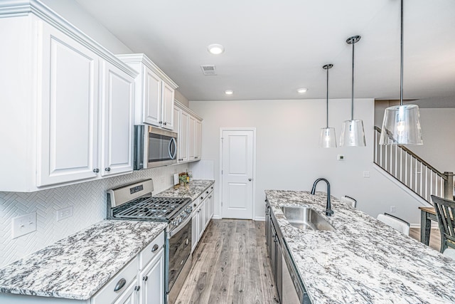 kitchen featuring a kitchen island with sink, white cabinets, sink, decorative light fixtures, and stainless steel appliances