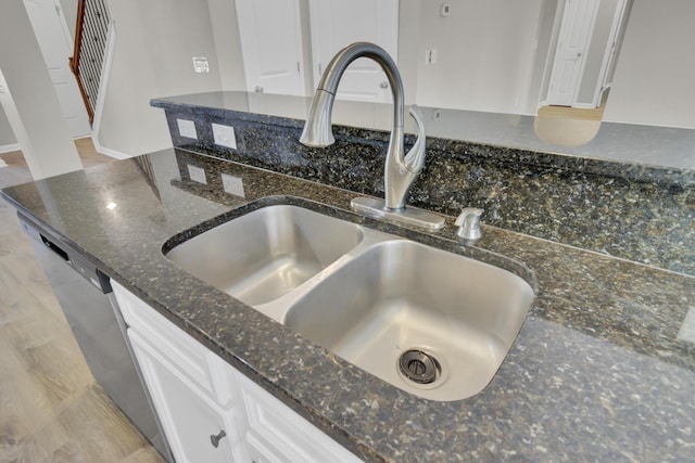 room details featuring sink, white cabinets, dark stone counters, and light hardwood / wood-style flooring