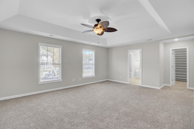 unfurnished bedroom featuring light carpet, ensuite bath, a raised ceiling, and ceiling fan