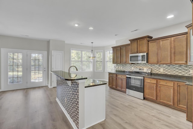 kitchen with tasteful backsplash, hanging light fixtures, stainless steel appliances, and light hardwood / wood-style floors