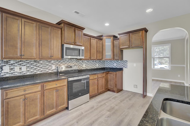 kitchen with dark stone countertops, decorative backsplash, light hardwood / wood-style floors, and appliances with stainless steel finishes