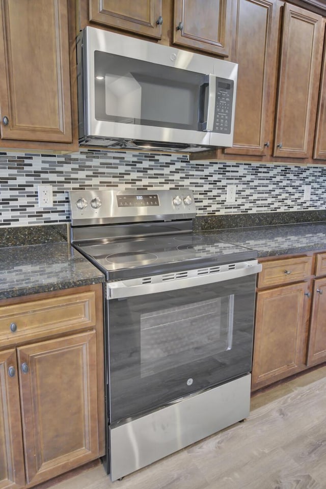 kitchen with dark stone countertops, tasteful backsplash, stainless steel appliances, and light hardwood / wood-style flooring