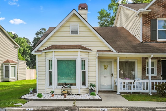 view of front of house with a shingled roof, a chimney, a porch, and a front yard