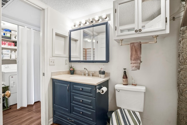 bathroom with a textured ceiling, wood finished floors, vanity, toilet, and washer / dryer