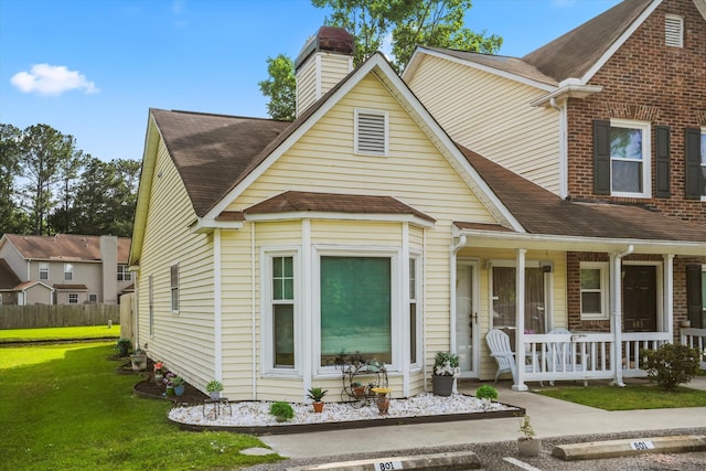 view of front of home with a porch, a shingled roof, a front yard, and a chimney