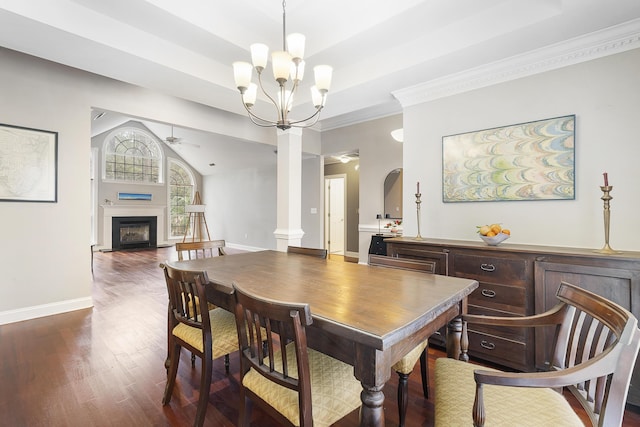 dining space featuring dark wood-type flooring, a fireplace, baseboards, a raised ceiling, and ornate columns