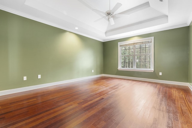 spare room featuring a tray ceiling, wood finished floors, a ceiling fan, and baseboards