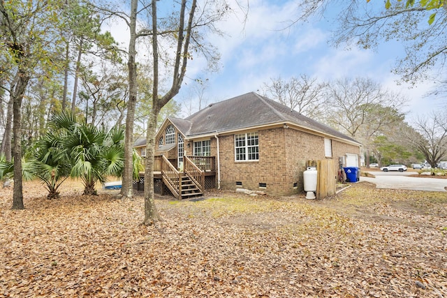 back of property with a deck, a garage, brick siding, crawl space, and stairway