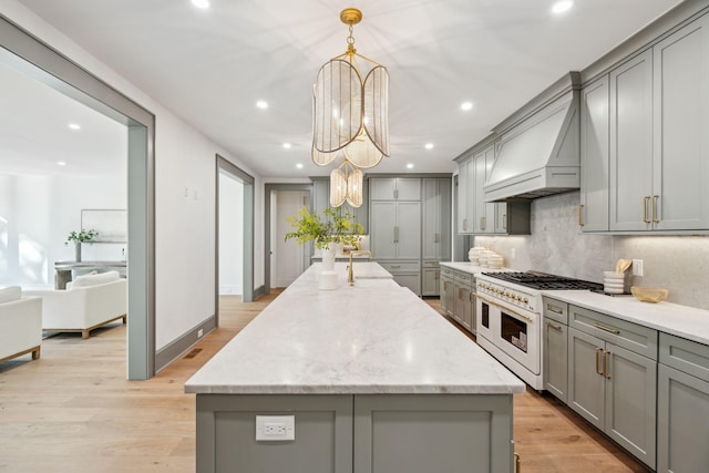 kitchen with light hardwood / wood-style floors, double oven range, gray cabinets, a spacious island, and premium range hood