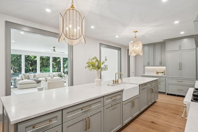 kitchen featuring sink, a kitchen island with sink, gray cabinets, light wood-type flooring, and decorative light fixtures