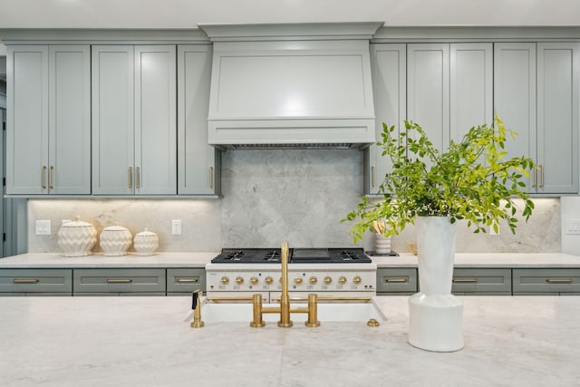 kitchen with gas stovetop, gray cabinetry, backsplash, light stone countertops, and premium range hood