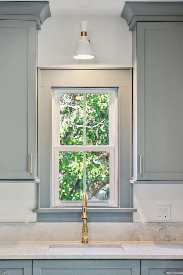 room details with gray cabinets, sink, and light stone countertops