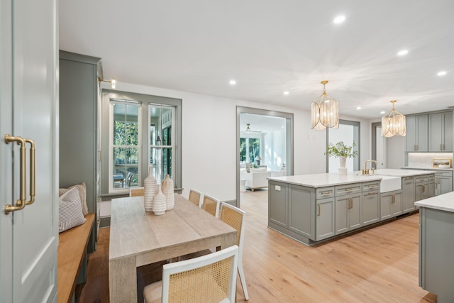 kitchen featuring gray cabinetry, light wood-type flooring, decorative light fixtures, sink, and a kitchen island with sink