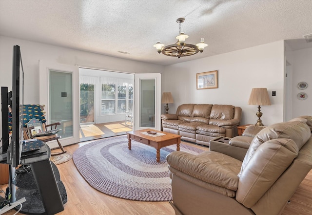 living room with a notable chandelier, a textured ceiling, and light hardwood / wood-style flooring