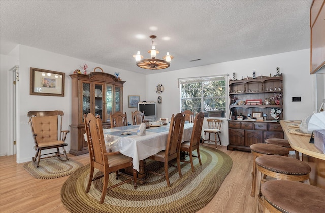 dining room with a chandelier, a textured ceiling, and light wood-type flooring