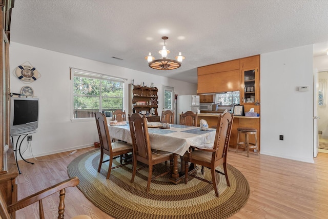 dining space featuring a textured ceiling, light wood-type flooring, and a notable chandelier