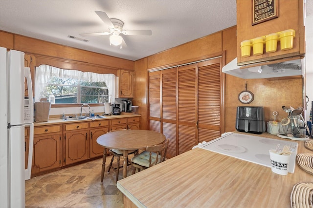 kitchen with cooktop, a textured ceiling, ceiling fan, sink, and white refrigerator