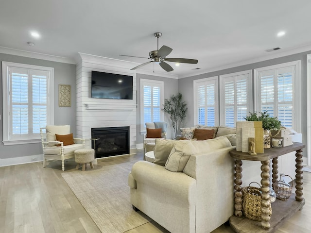 living room with ceiling fan, a large fireplace, crown molding, and light hardwood / wood-style flooring