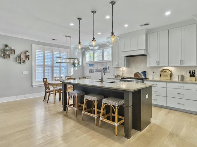 kitchen featuring light stone countertops, sink, pendant lighting, white cabinetry, and an island with sink