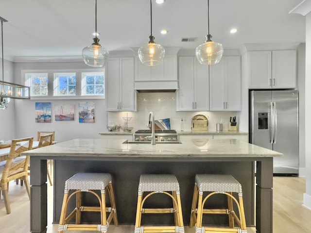 kitchen featuring white cabinets, stainless steel fridge, an island with sink, and light stone countertops