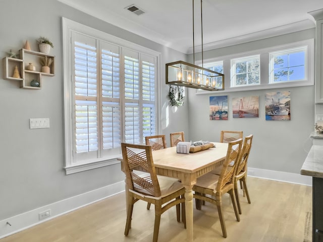 dining area featuring light wood-type flooring, ornamental molding, and an inviting chandelier