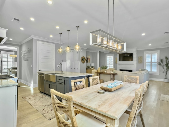 dining area featuring a fireplace, crown molding, sink, and light wood-type flooring