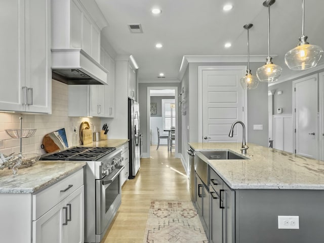 kitchen featuring premium range hood, white cabinets, decorative light fixtures, and appliances with stainless steel finishes