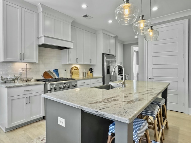 kitchen featuring a kitchen island with sink, white cabinets, hanging light fixtures, and light stone counters