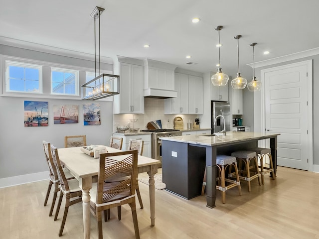 kitchen featuring light wood-type flooring, stainless steel appliances, a kitchen island with sink, decorative light fixtures, and white cabinetry