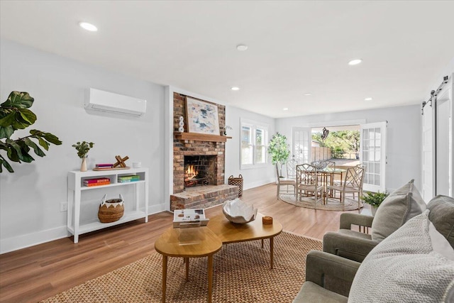 living room with a barn door, a wall unit AC, light hardwood / wood-style flooring, and a fireplace