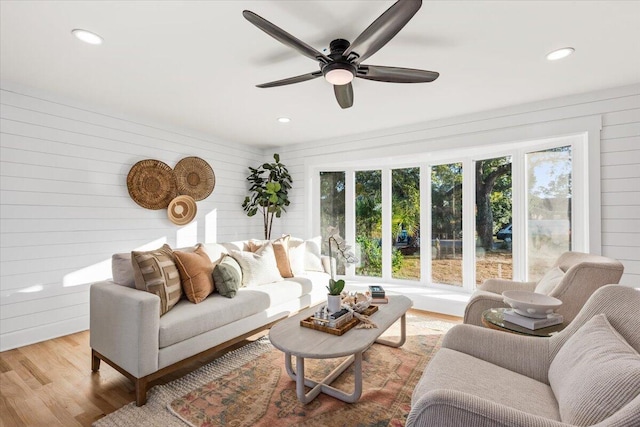 living room with light hardwood / wood-style floors, ceiling fan, wooden walls, and a wealth of natural light