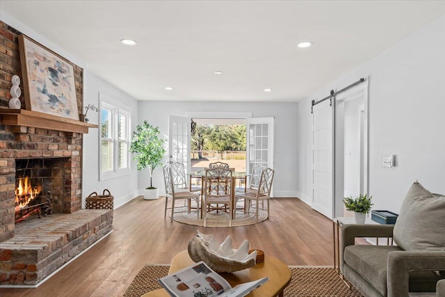 living room with a barn door, a brick fireplace, and hardwood / wood-style flooring