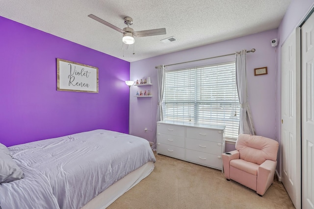 bedroom featuring visible vents, light carpet, a textured ceiling, a closet, and ceiling fan