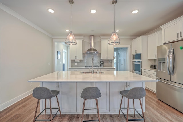 kitchen with white cabinets, wall chimney exhaust hood, stainless steel appliances, and pendant lighting