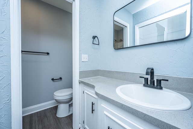 bathroom featuring vanity, toilet, wood finished floors, a textured wall, and baseboards