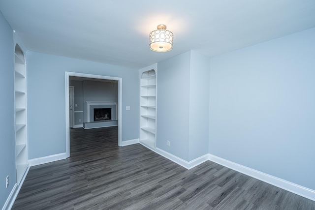 unfurnished room with built in features, baseboards, dark wood-type flooring, and a fireplace with raised hearth